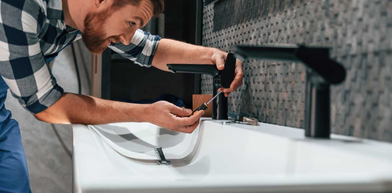 A plumber fitting a faucet on a bathroom sink, standing in for the homeowner who quietly researches a plumber through an AI answer before making the call.